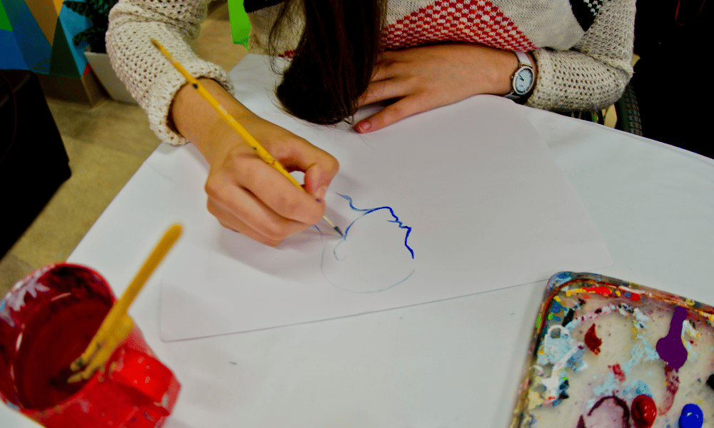 Young child paints the blue outline of a side portrait. Photo credited to Phil Bayly