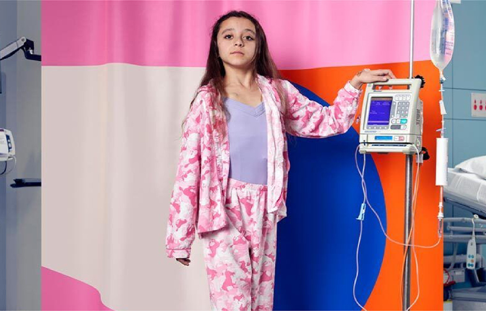 Young girl in pajamas standing next to a piece of hospital equipment in a ward