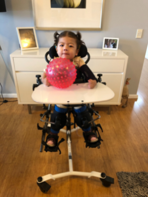 Lucia sitting in a supportive high chair with a pink bouncy ball