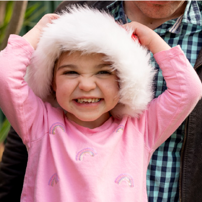 Abigail outside sitting on her dad's lap. She is wearing a fluffly christmas hat and a pink sweater with rainbows on it Abigail outside sitting on her dad's lap. She is wearing a fluffly christmas hat and a pink sweater with rainbows on it