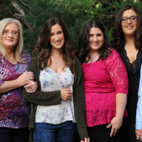 Four women standing together in front of green trees