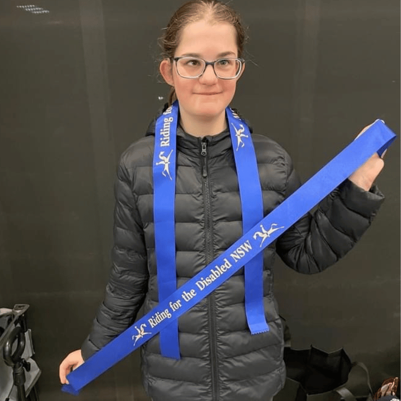 Chloe holding her ribbon for becoming champion in the Riding for the Disabled State Dressage Championships