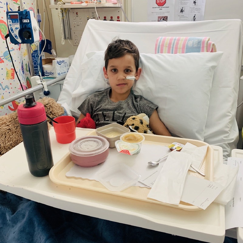 Hugo sitting up in his hospital bed, holding a stuffed tiger toy.