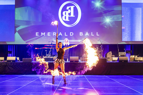 A fire dancer with flaming torches performing on stage at Emerald Ball 2025