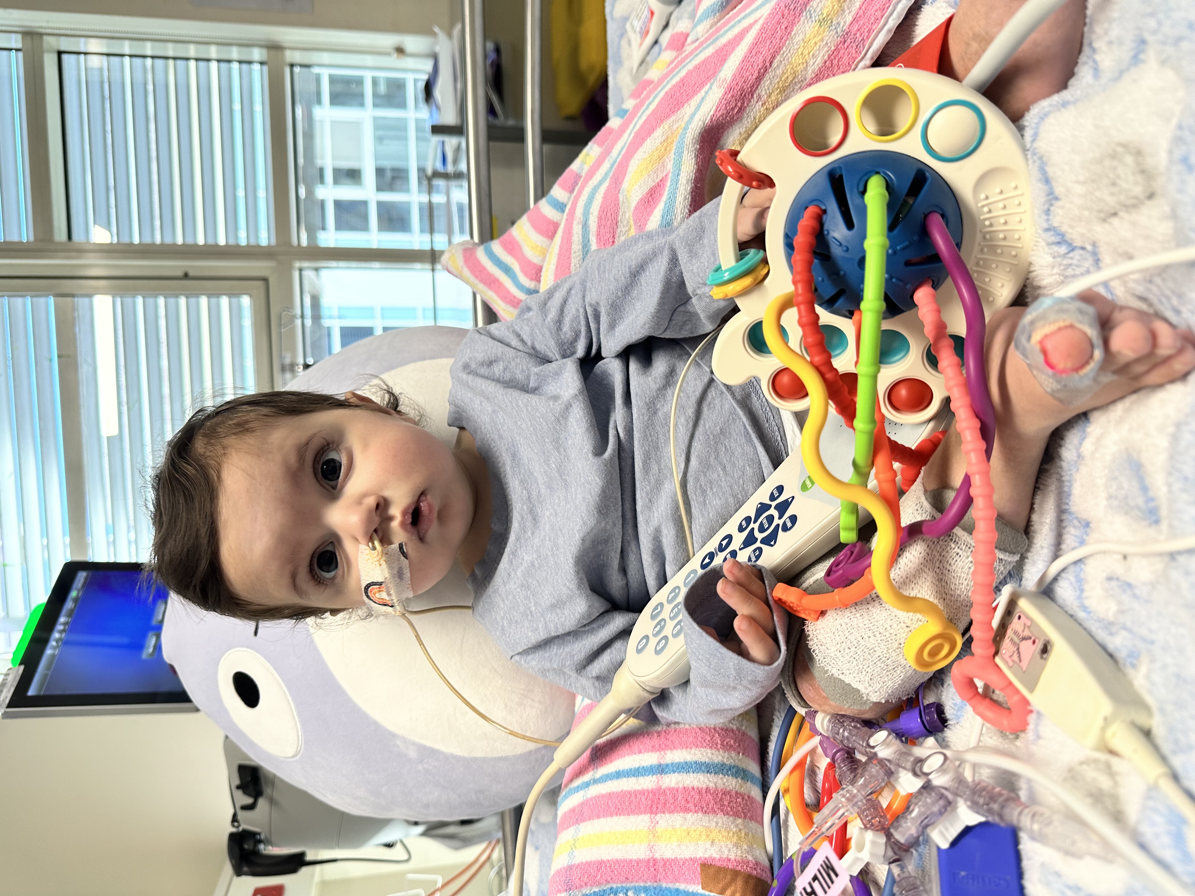 Image of baby sitting up in hospital bed with toys.