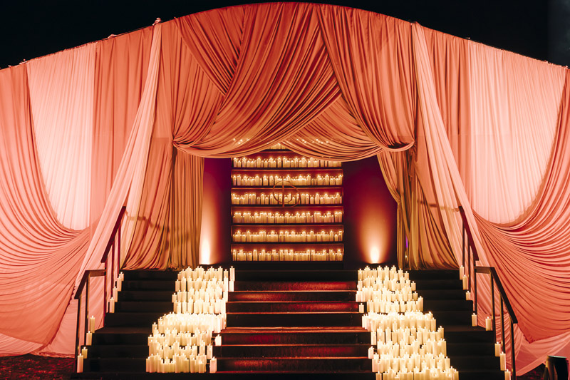 An elegantly decorated stairway lined with hundreds of glowing candles and an arch draped with bright red cloth