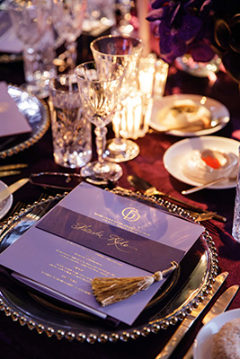 A table setting at Gold Dinner 2025. Elegant wine glasses, gold rimmed dinner plates and a calligraphy adorned evening program can be seen.