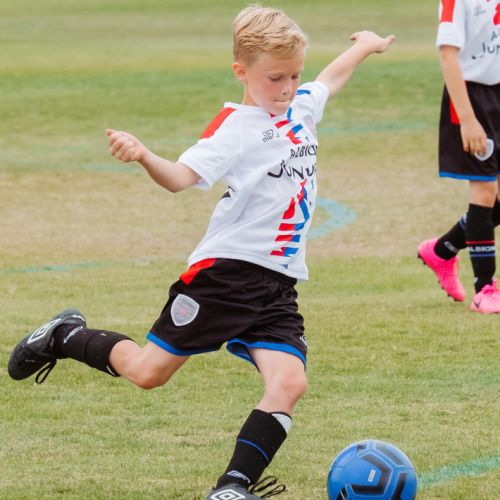 A young boy in a white and black soccer kit kicking a blue soccer ball