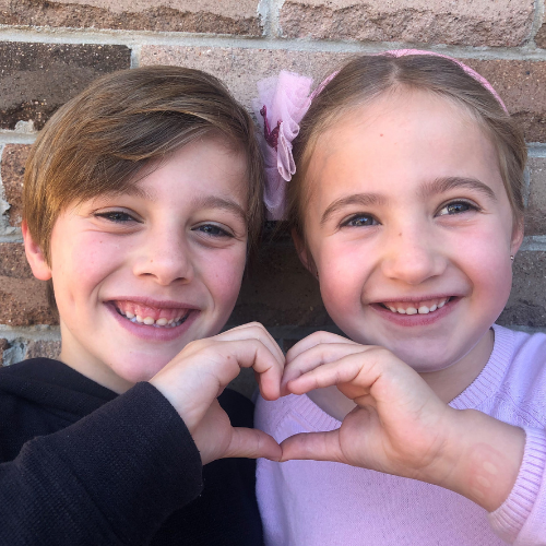 A young boy and girl smiling and holding their hands together to make a heart symbol