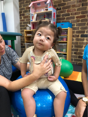 Lucia sitting on a physiotherapy ball being supported by a physiotherapist