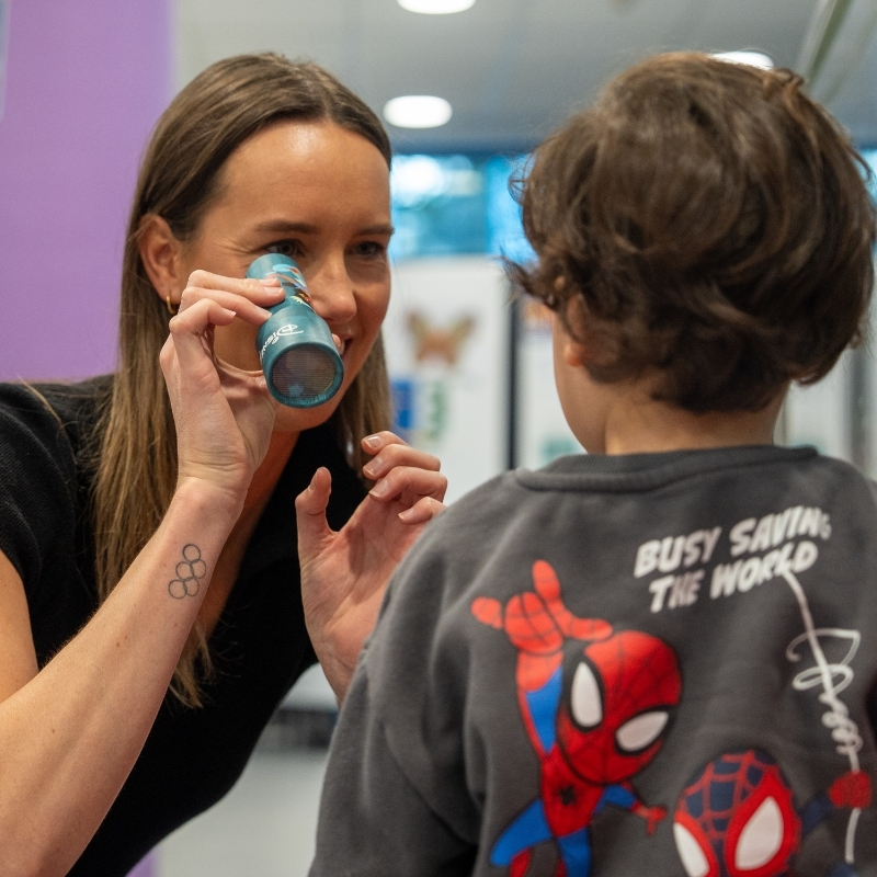 Emma Mckeon holding a torch up in front of her face while playing with a child in hospital