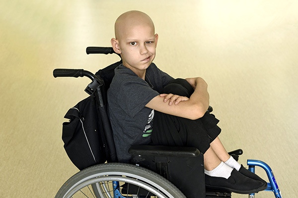 Caleb during treatment in the hospital sitting with his arms crossed and legs curled up in a wheelchair.