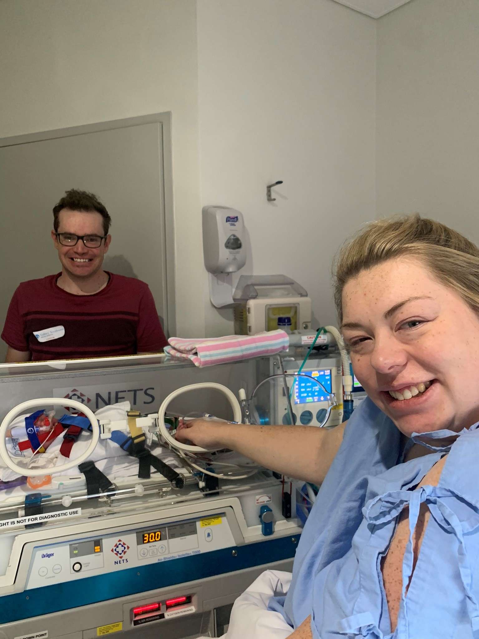 Image of parents on either side of humidicrib with hand in touching baby.