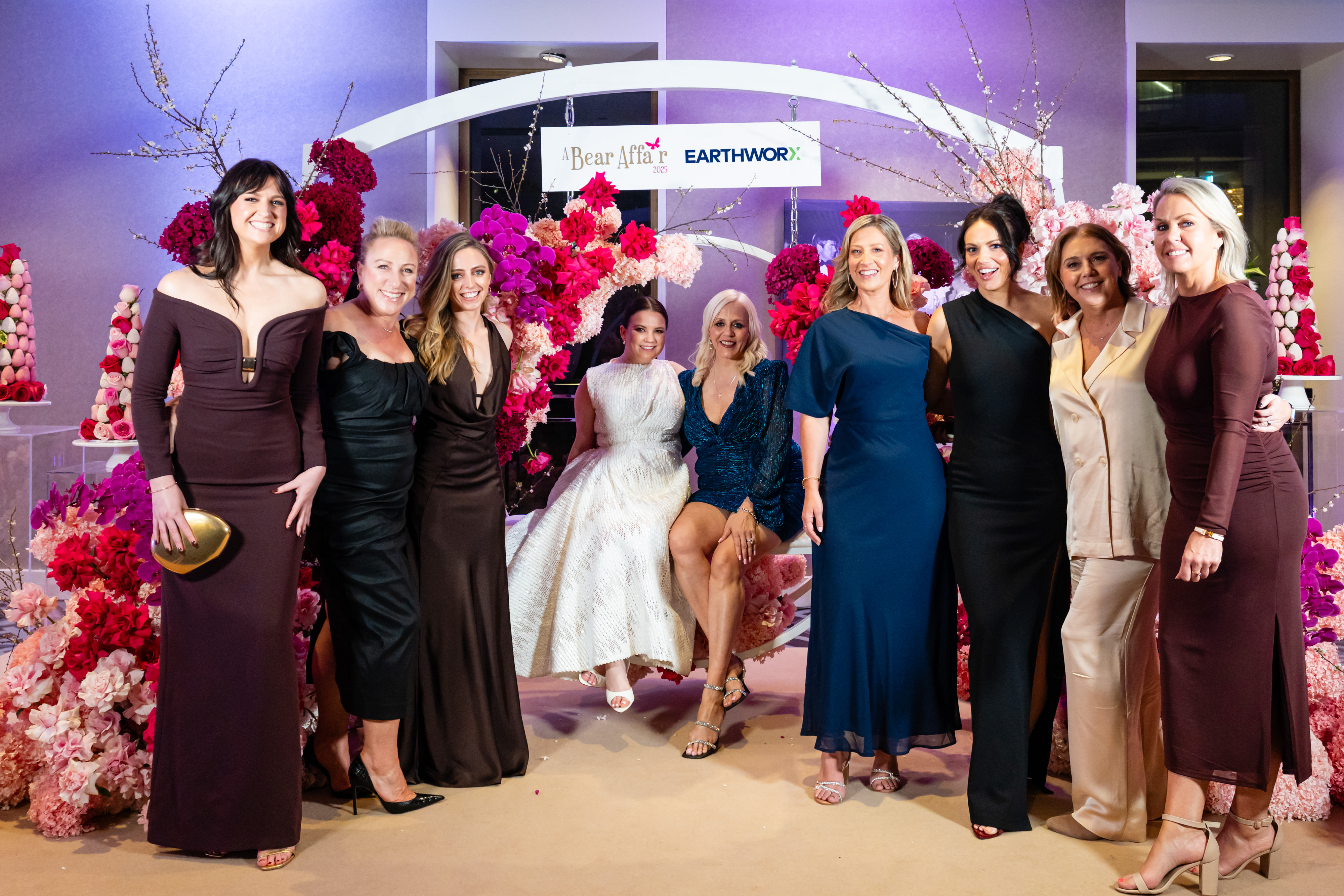 A group of guests posing on a decorative swing framed by pink flowers.