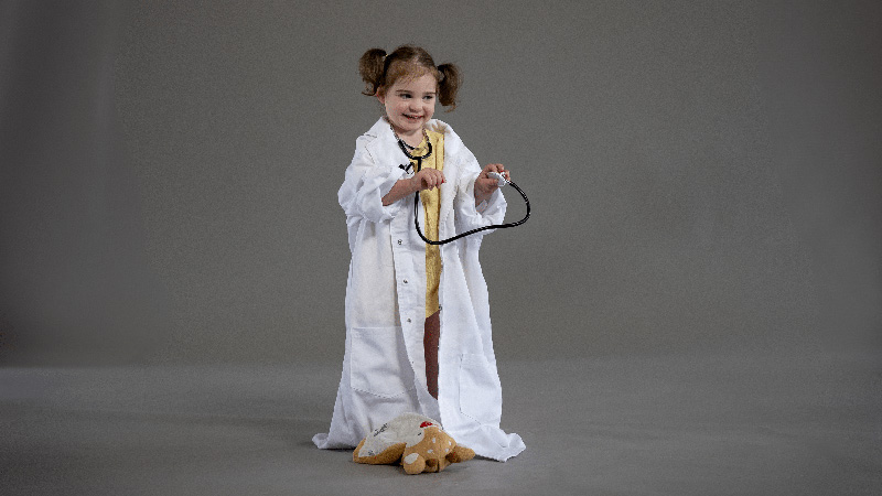 A young girl wearing a white oversized doctor coat and holding a stethoscope