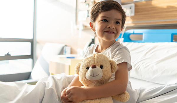 A young boy sitting on a hospital bed with a teddy bear in his lap A young boy sitting on a hospital bed with a teddy bear in his lap