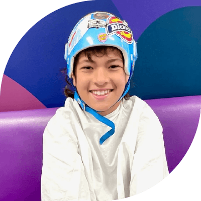 Remy looking happy as he sits on a purple seat in a white hopsital gown. he's wearing a blue medical helmet on his head.