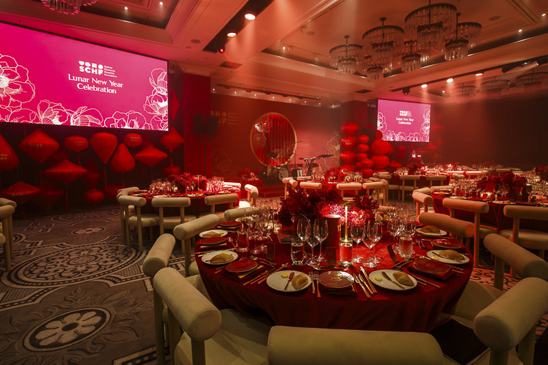 The room before attendees arrive. Many colourfully decorated dining tables can be seen with red lights and two large TV screens on the back wall