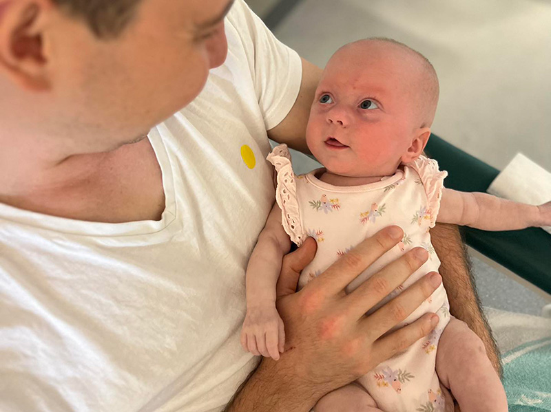 Aria's dad holding her as a newborn. her big eyes are looking up at him lovingly