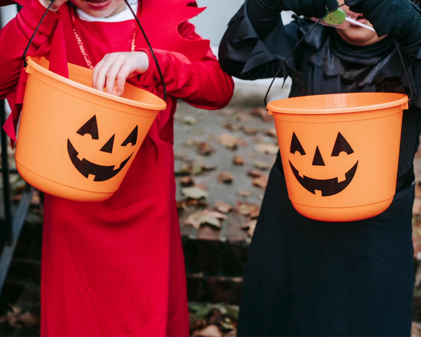 'Two children in Halloween costumes holding jack-o'-lantern buckets on a leaf-covered path. 'Two children in Halloween costumes holding jack-o'-lantern buckets on a leaf-covered path.