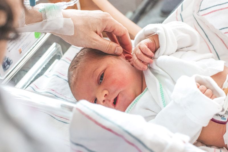 Newborn baby in hospital cot holding an adult’s finger