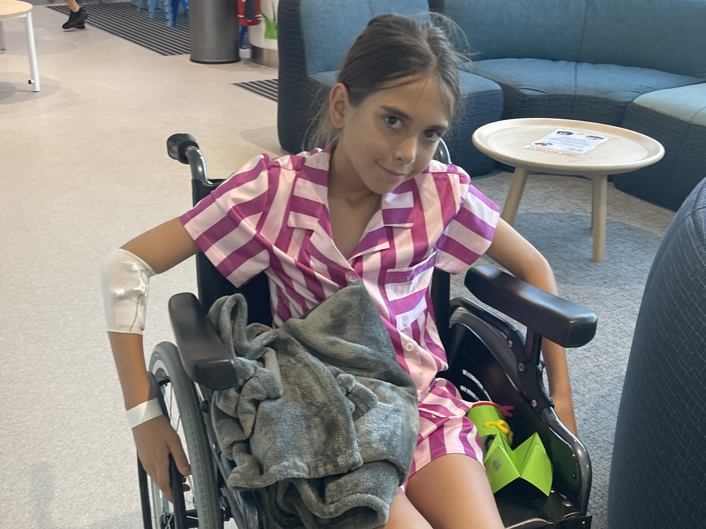 Child sitting in a wheelchair, wearing striped pyjamas with an IV bandage on their arm.