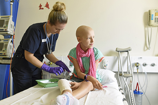 Eve during treatment sitting on a hospital bed while a nurse wearing gloves performs a medical procedure