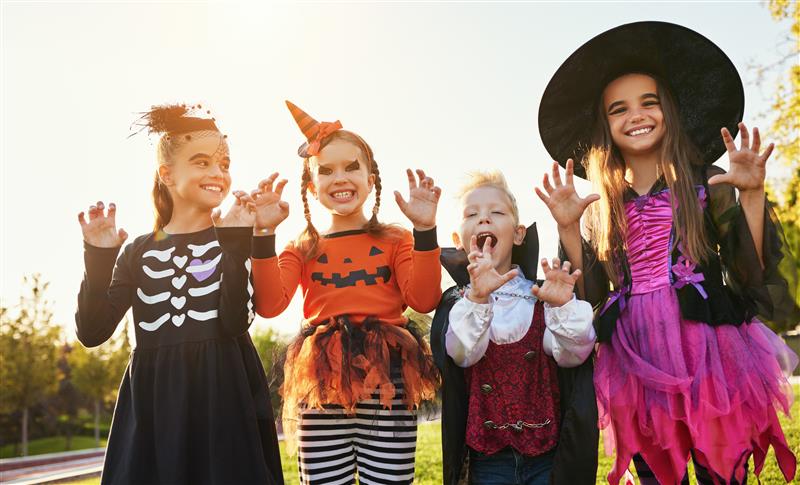 Four children in Halloween costumes posing playfully outdoors.