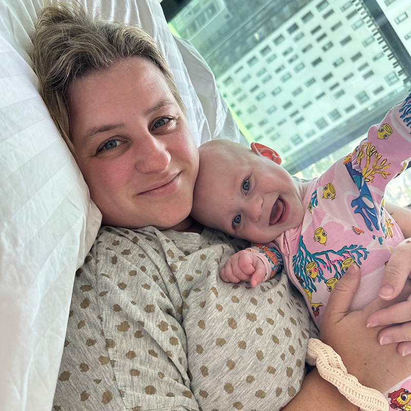 Aria and her mum in bed cuddling. Aria has a big smile and her hand held in the air