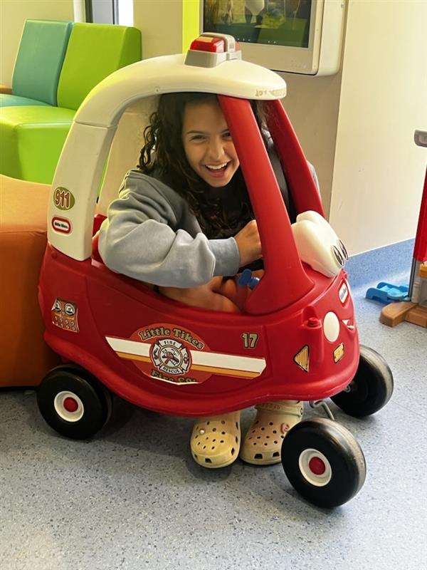 Tayla squashed into in a kids fire engine toy car with a big grin on her face