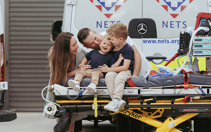 Pictured: Koby and Cooper with their parents Michael and Amanda smiling and laughing while the boys sit on a NETS hospital stretcher