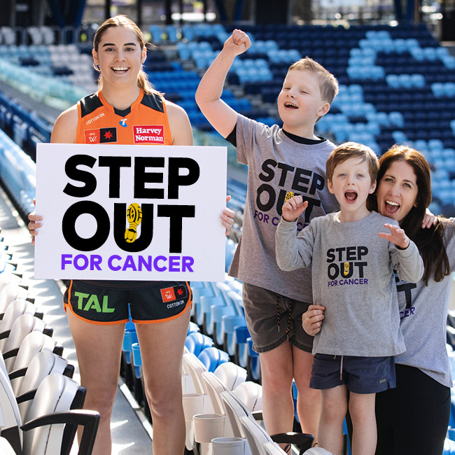 a GWS giants player standing in a stadium seating area holding a sign with a family of 3 cheering them on the side. the sign says 'Step Out for Cancer'