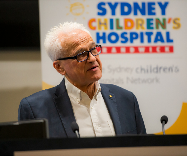 Professor Les White speaking at a podium. Behind him is a banner with Sydney Children's Hospital, Randwick's logo on it.