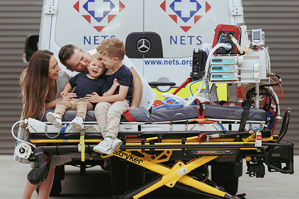 Koby and Cooper with their parents sitting on a NETS mobile hospital bed with NETS vehicles behind them Koby and Cooper with their parents sitting on a NETS mobile hospital bed with NETS vehicles behind them