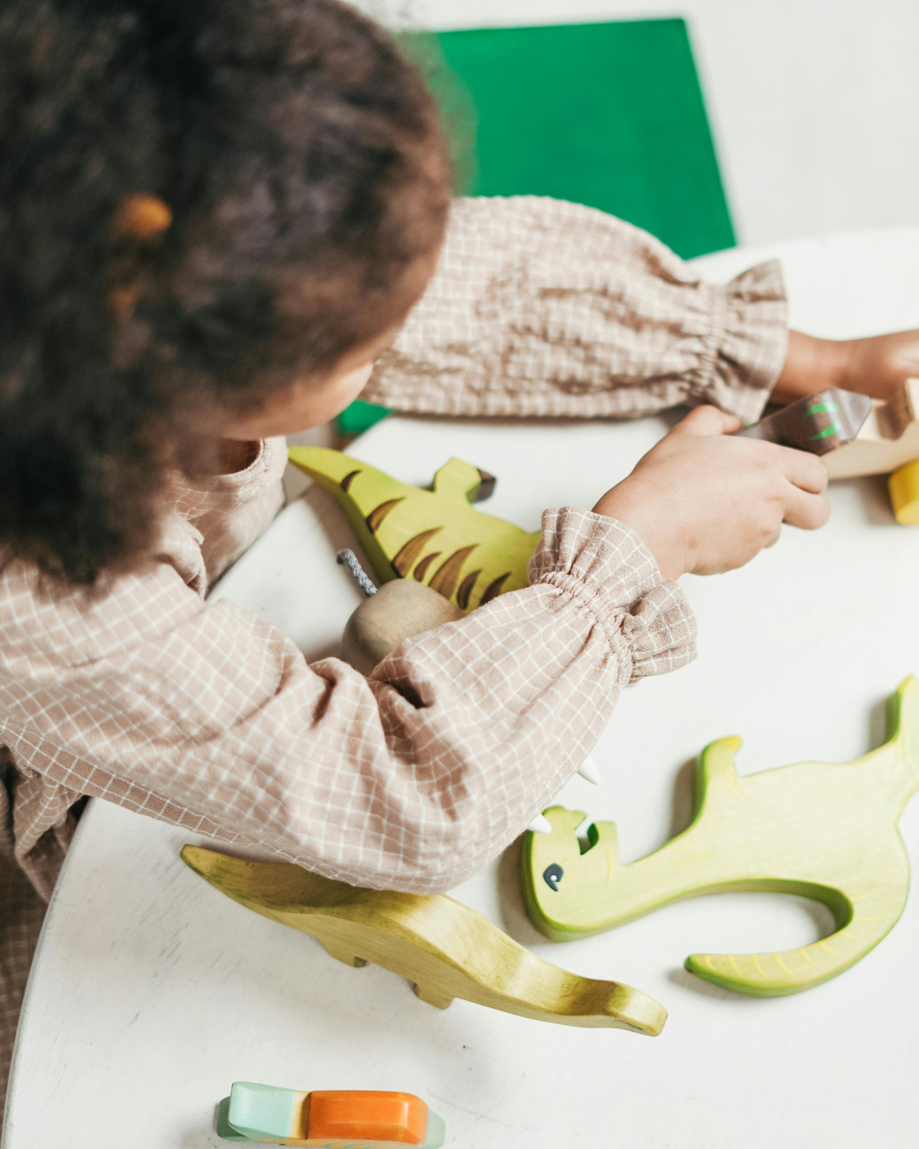 Image of from above of child sitting down at table playing with wooden toys. Image of from above of child sitting down at table playing with wooden toys.