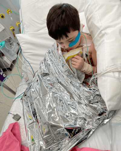 Cooper in hospital wrapped in a heat blanket with many tubes and wires connected to him.
