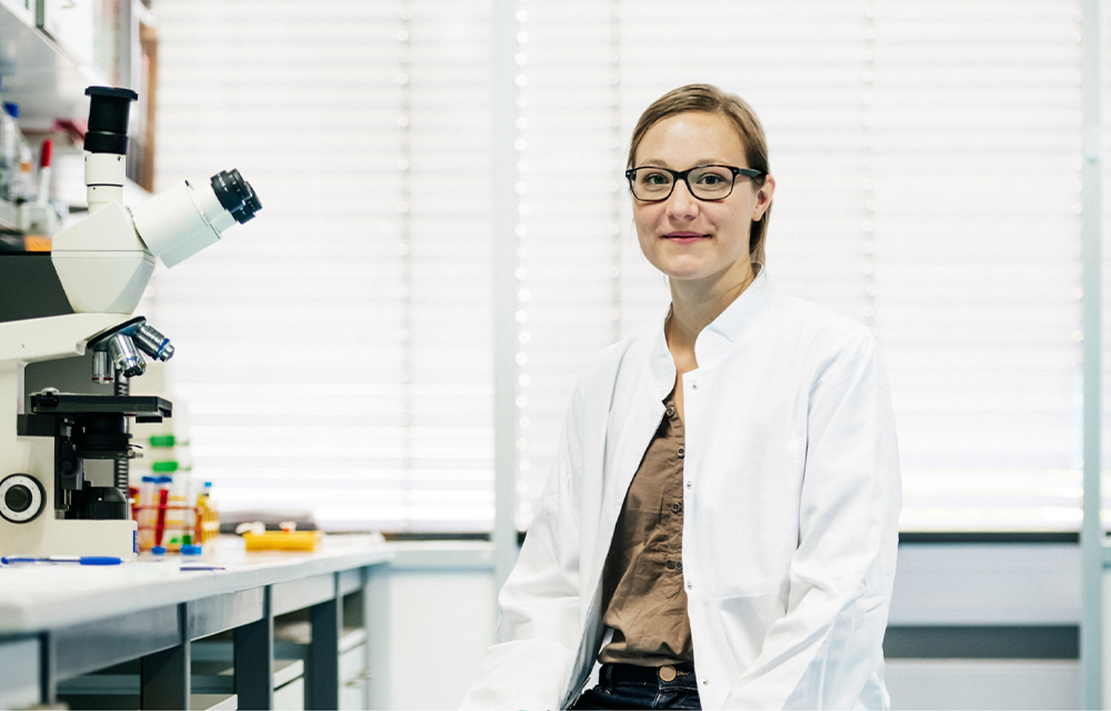 Female scientist sitting next to a telescope in a lab