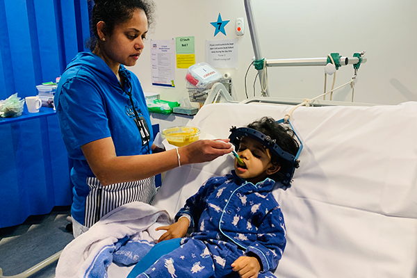 Kiveyn's mum feeding him some food while he lays in a hospital bed