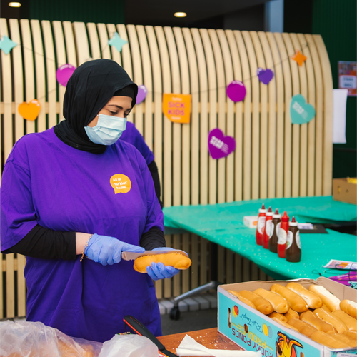 A volunteer cutting a hotdog bun