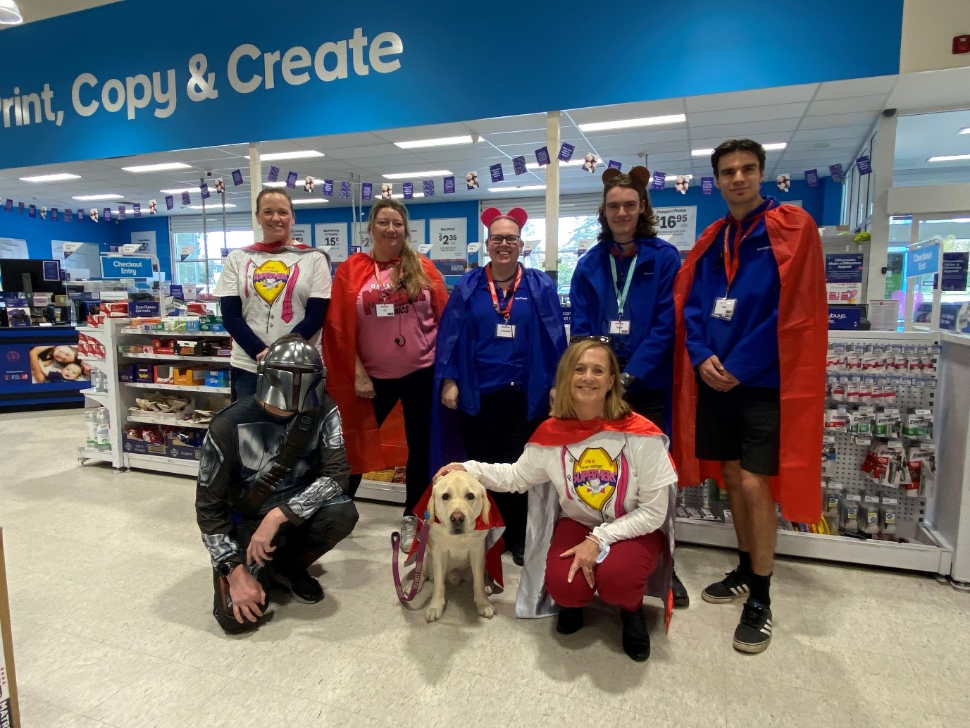 Officeworks staff dressed up as superheroes and a Labrador wearing a superhero cape